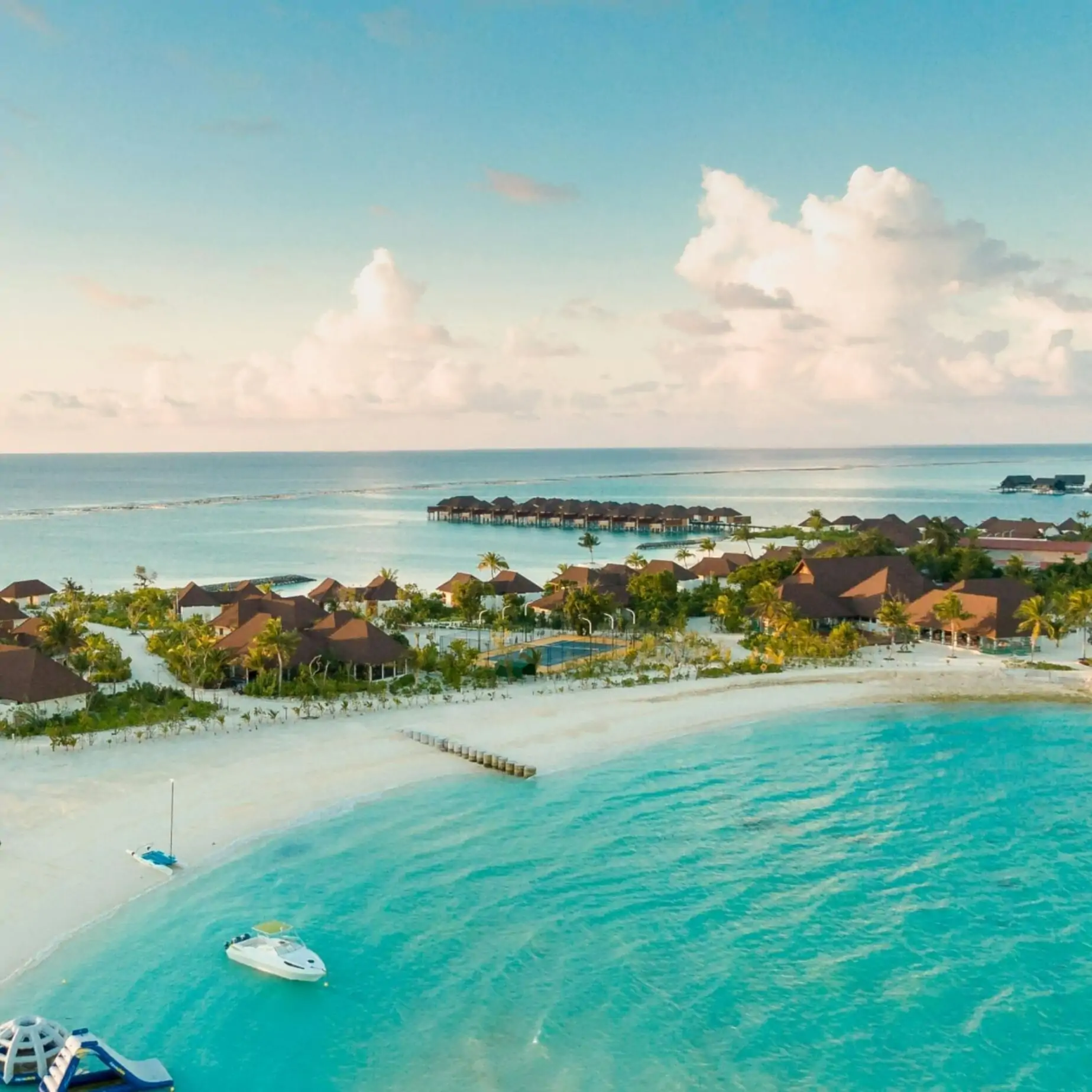 An aerial view of a tropical resort with beachfront villas, turquoise water under a clear sky.