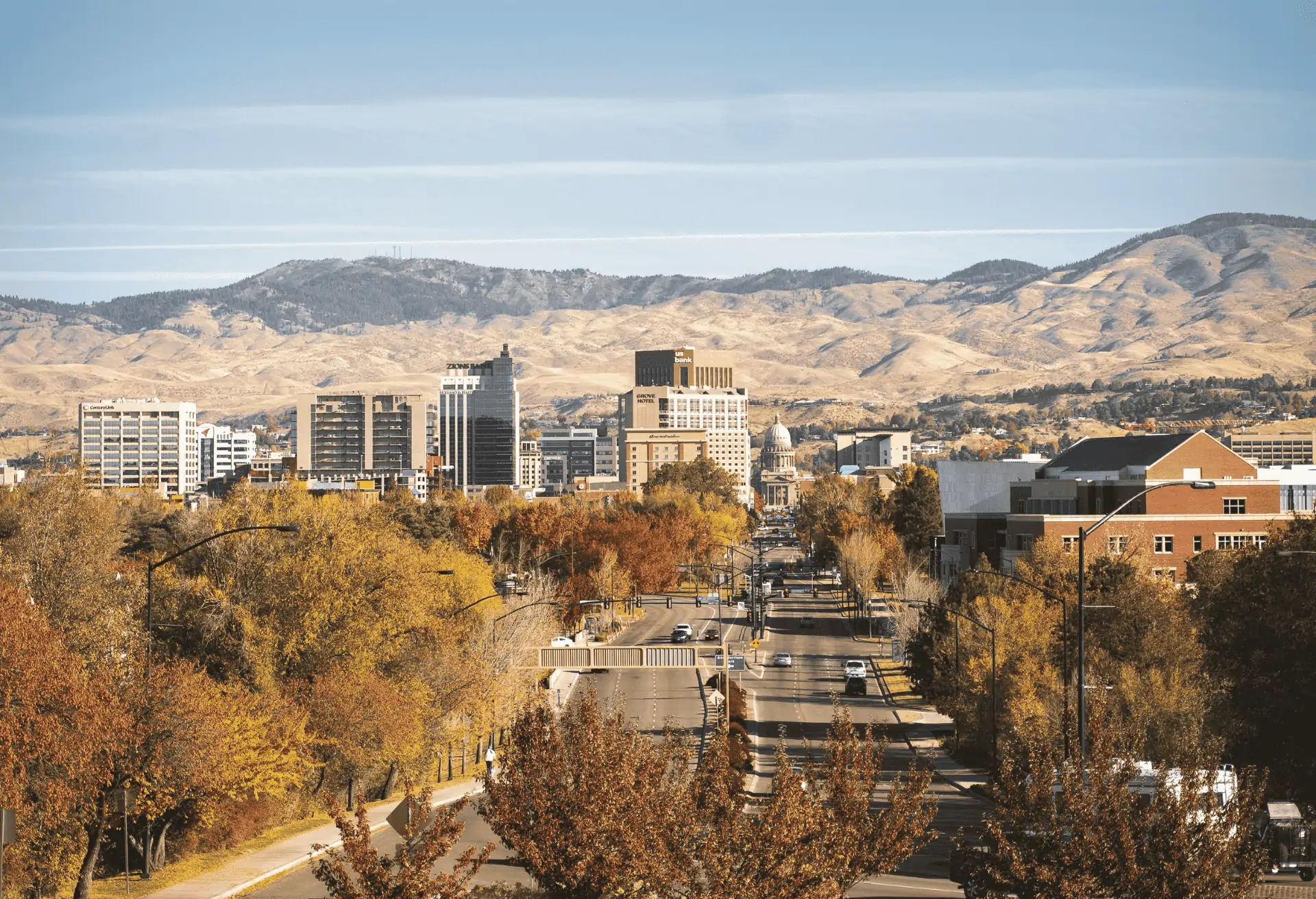 A panoramic view of Boise, Idaho, on a clear day, showing a mix of modern buildings in the city center against a backdrop of rolling, dry hills.