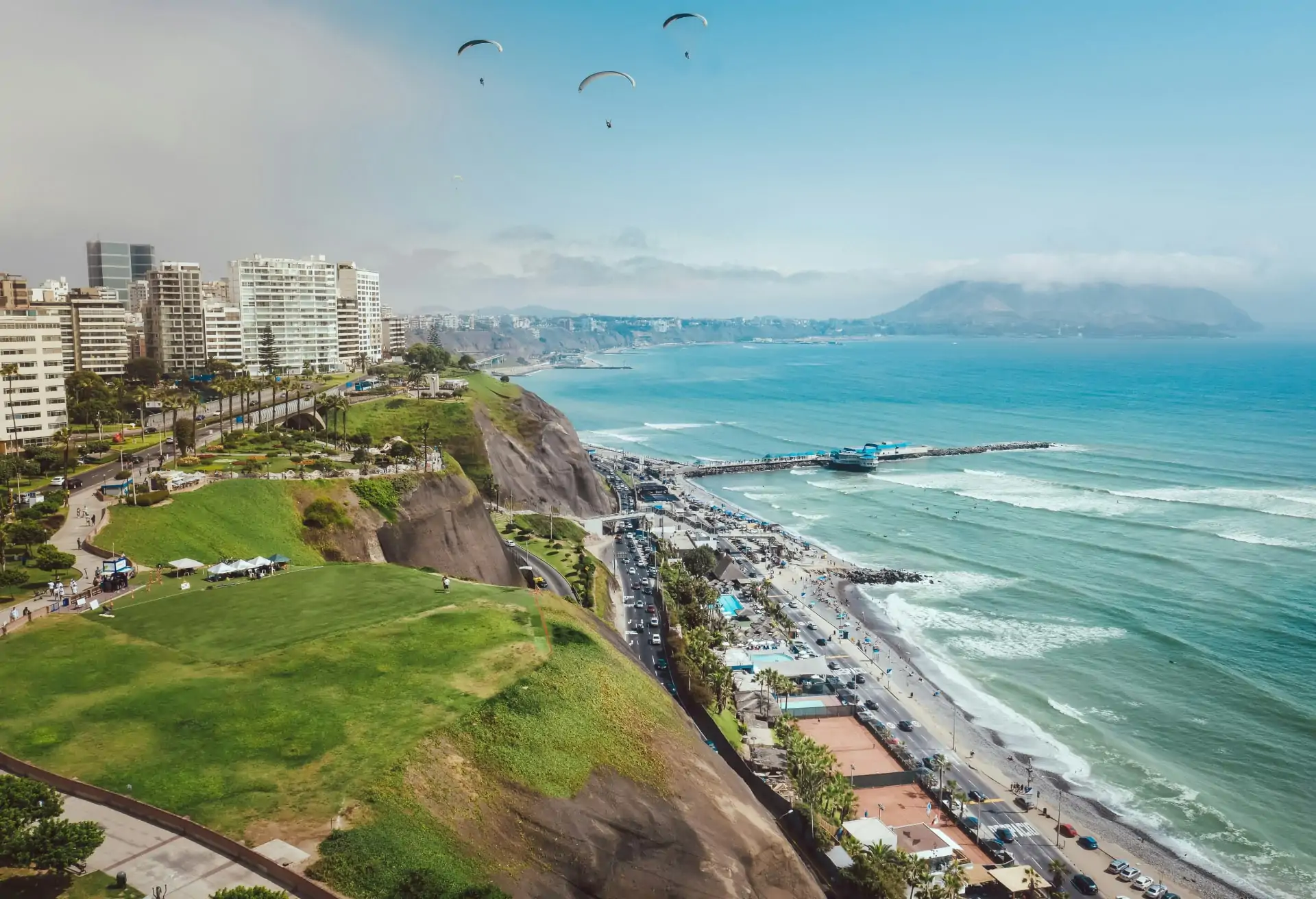 An aerial view of Lima’s coastline with modern buildings on green cliffs overlooking the Pacific Ocean.