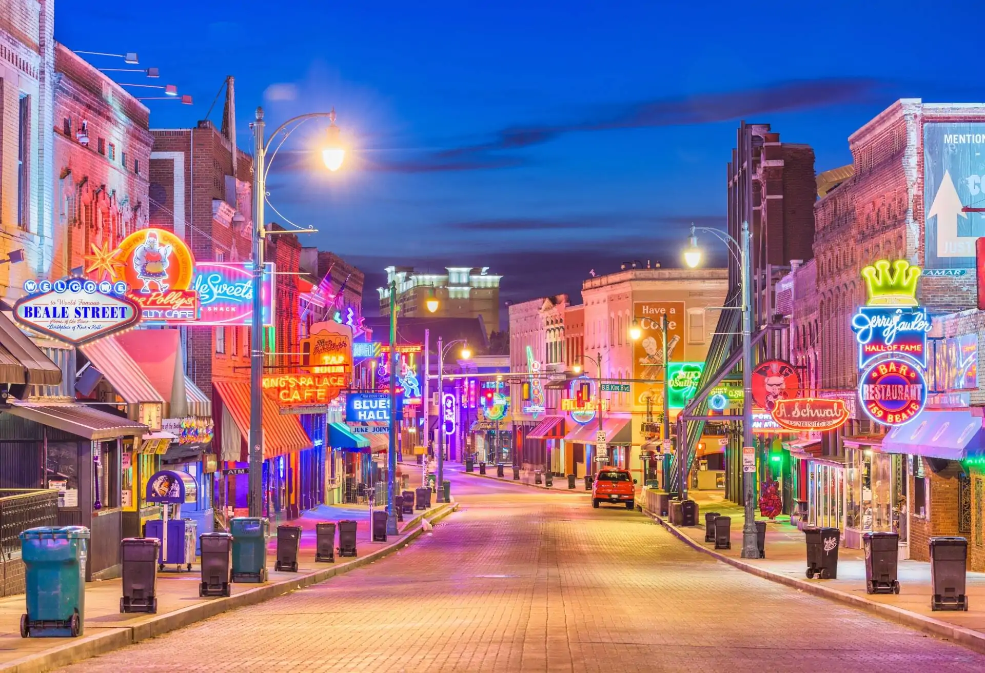 A view of an empty road in Downtown Memphis at night featuring buildings with colorful signs and lights on either side of the road.