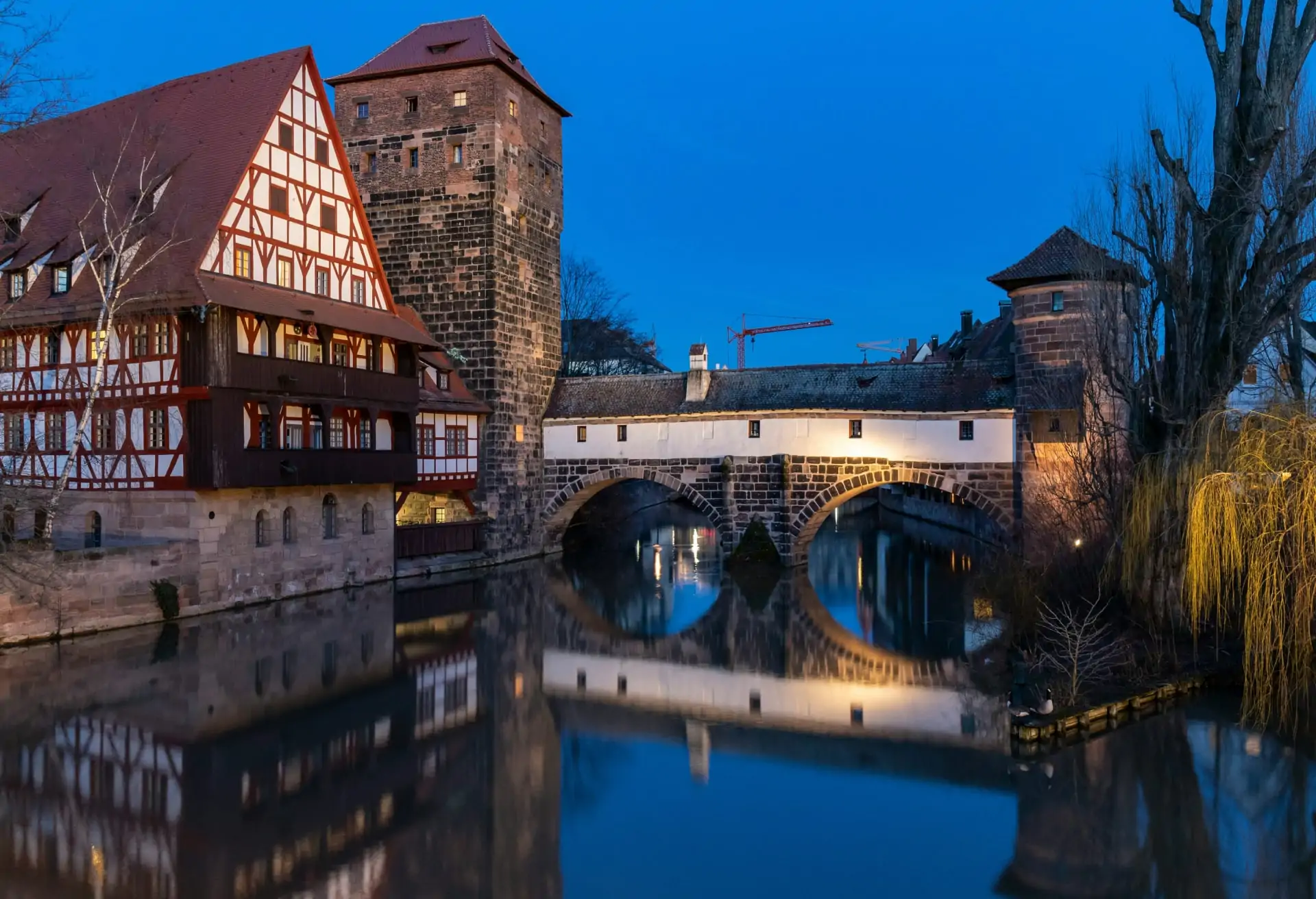 A view of Nuremberg’s old town with traditional Bavarian architecture at night. There is also a river with a cobblestone bridge across it.