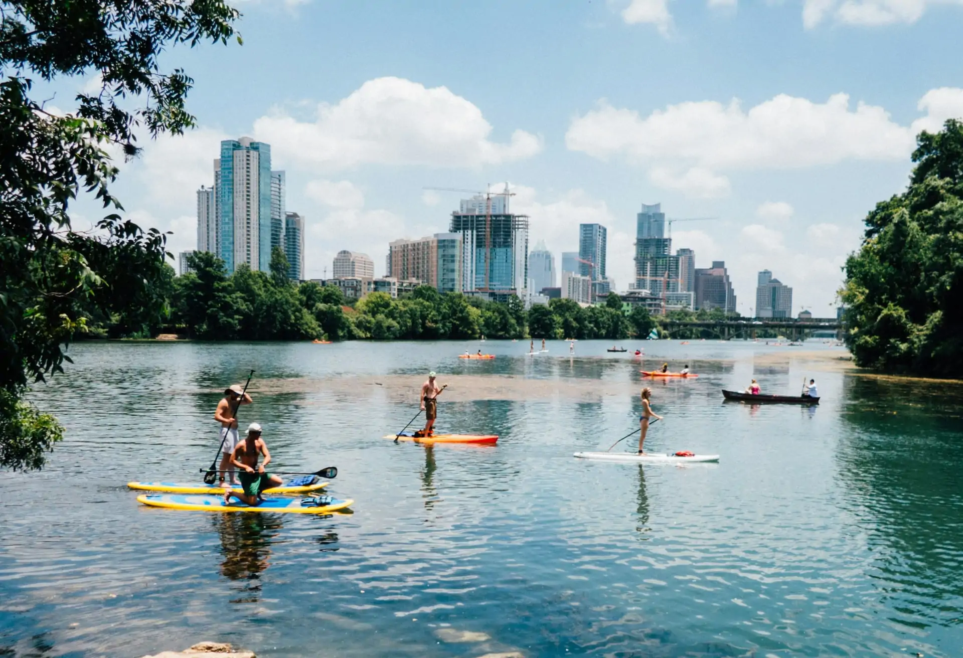 A lively view of Austin’s downtown area with modern skyscrapers and the Colorado River in the foreground, set against a bright blue sky.