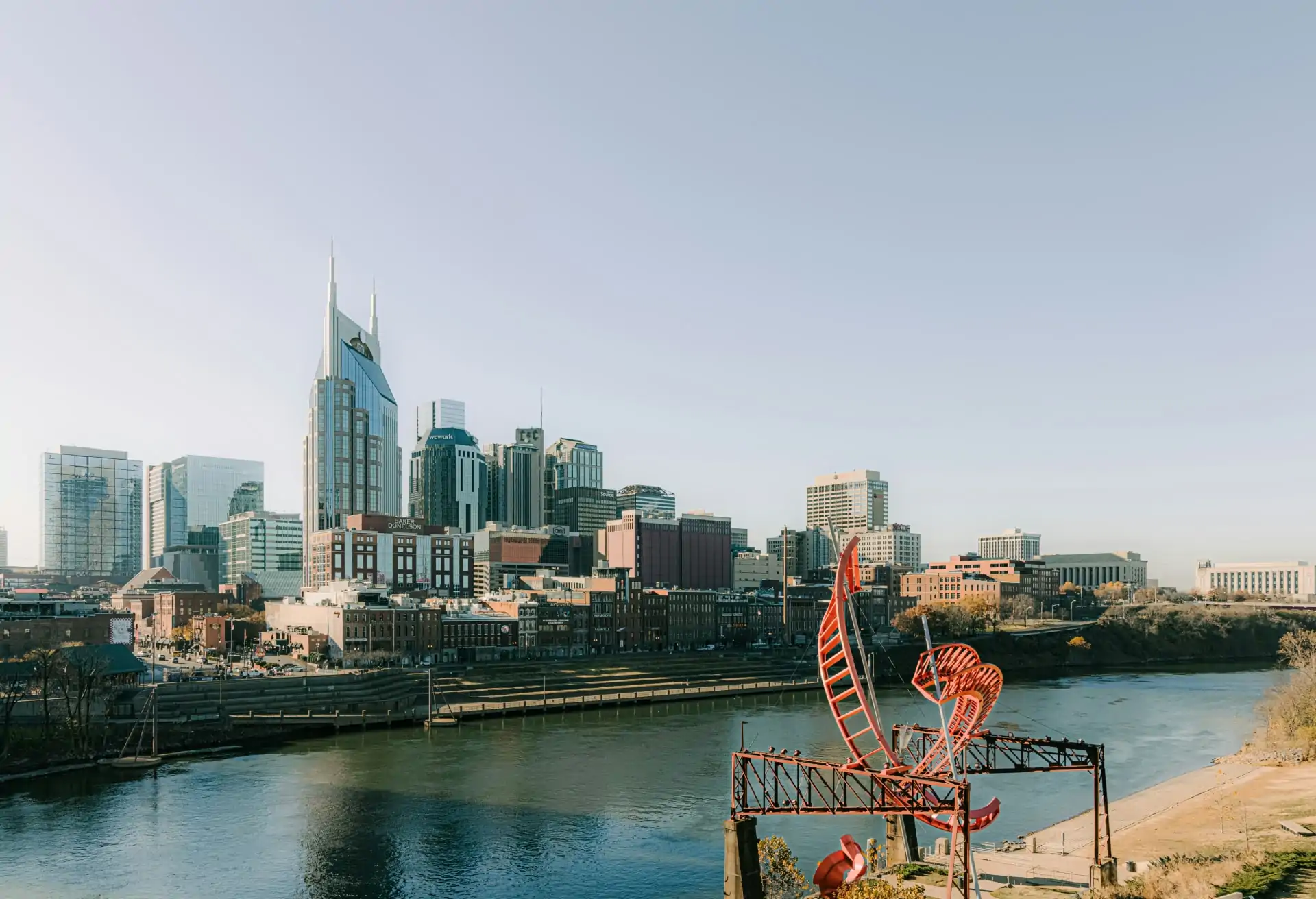 A view of central Nashville with modern buildings and skyscrapers with a river in the foreground.