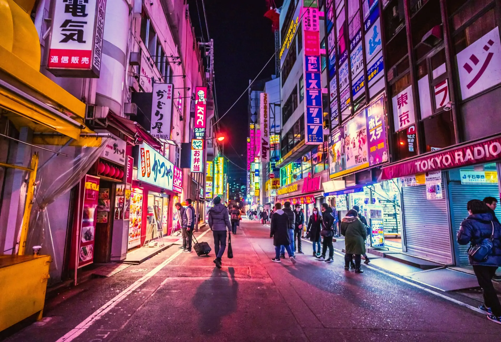 A view of a street in Tokyo with a few people, colorful signs and neon lights.