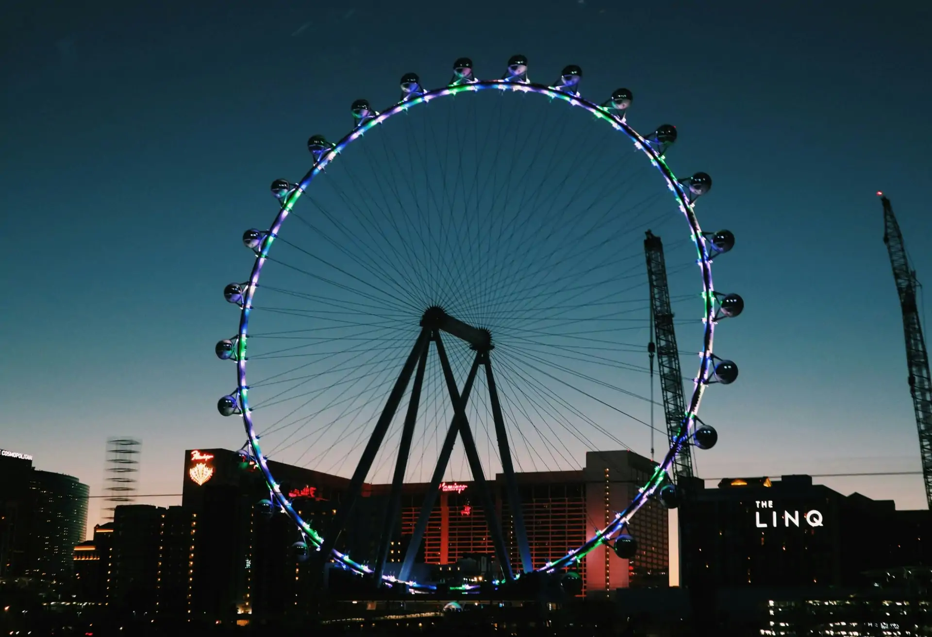 A night view of Las Vegas’ featuring a Ferris wheel with blue and green lights.