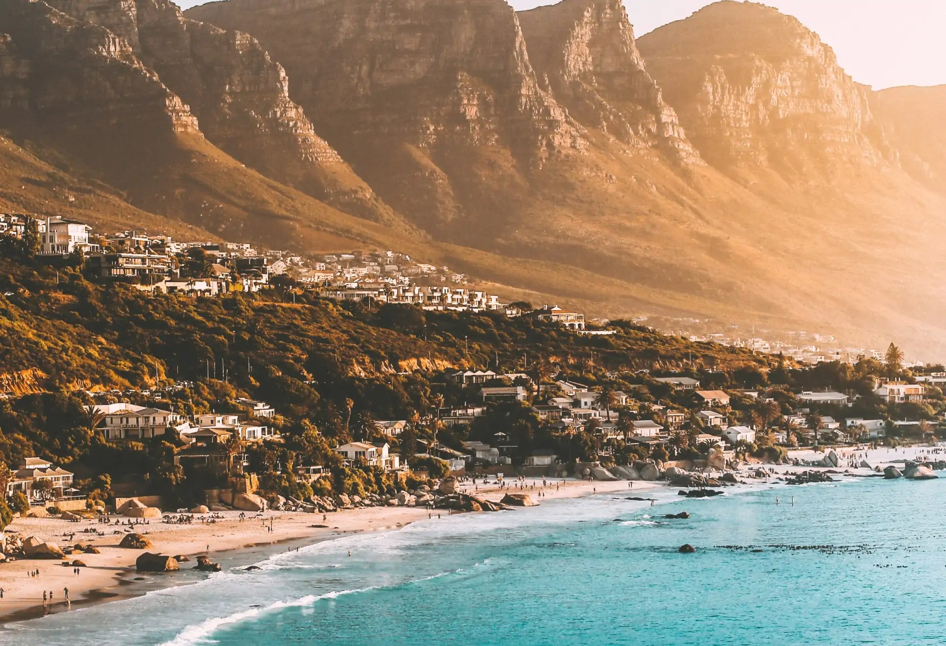 A view of Cape Town's coastline with buildings and greenery leading down to a blue sea with mountains in the background.