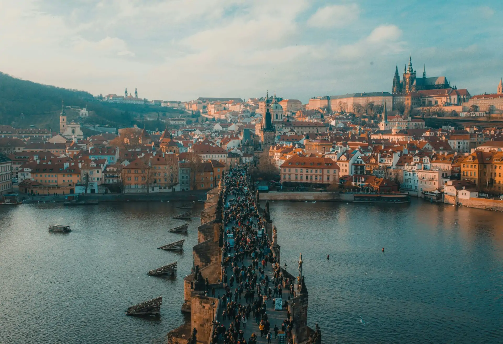 A view of Prague’s historic city center with medieval buildings and lots of people on the Charles Bridge over the river.