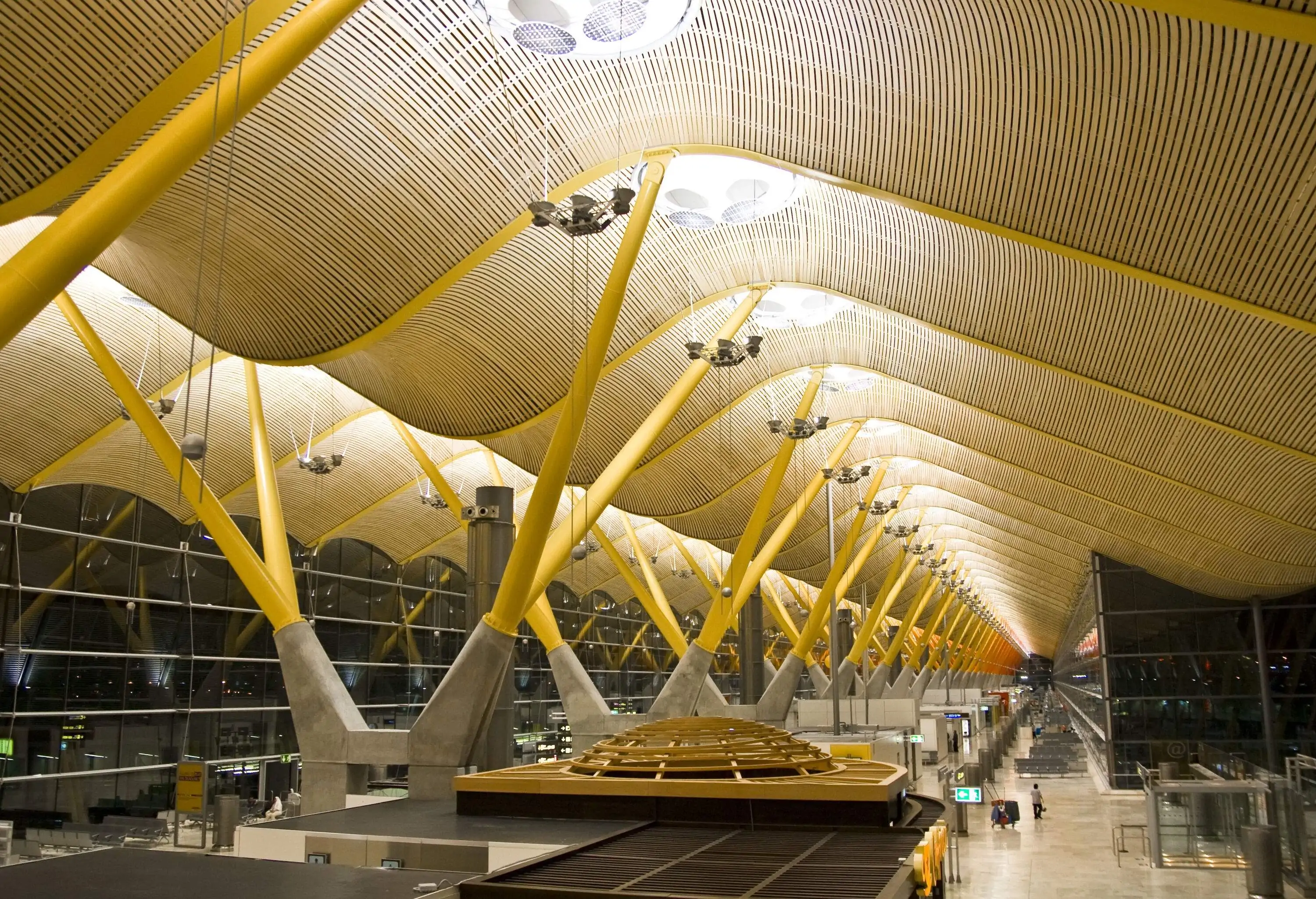 A brightly lit airport terminal supported by multiple orange pillars with a ceiling in the shape of a wave.