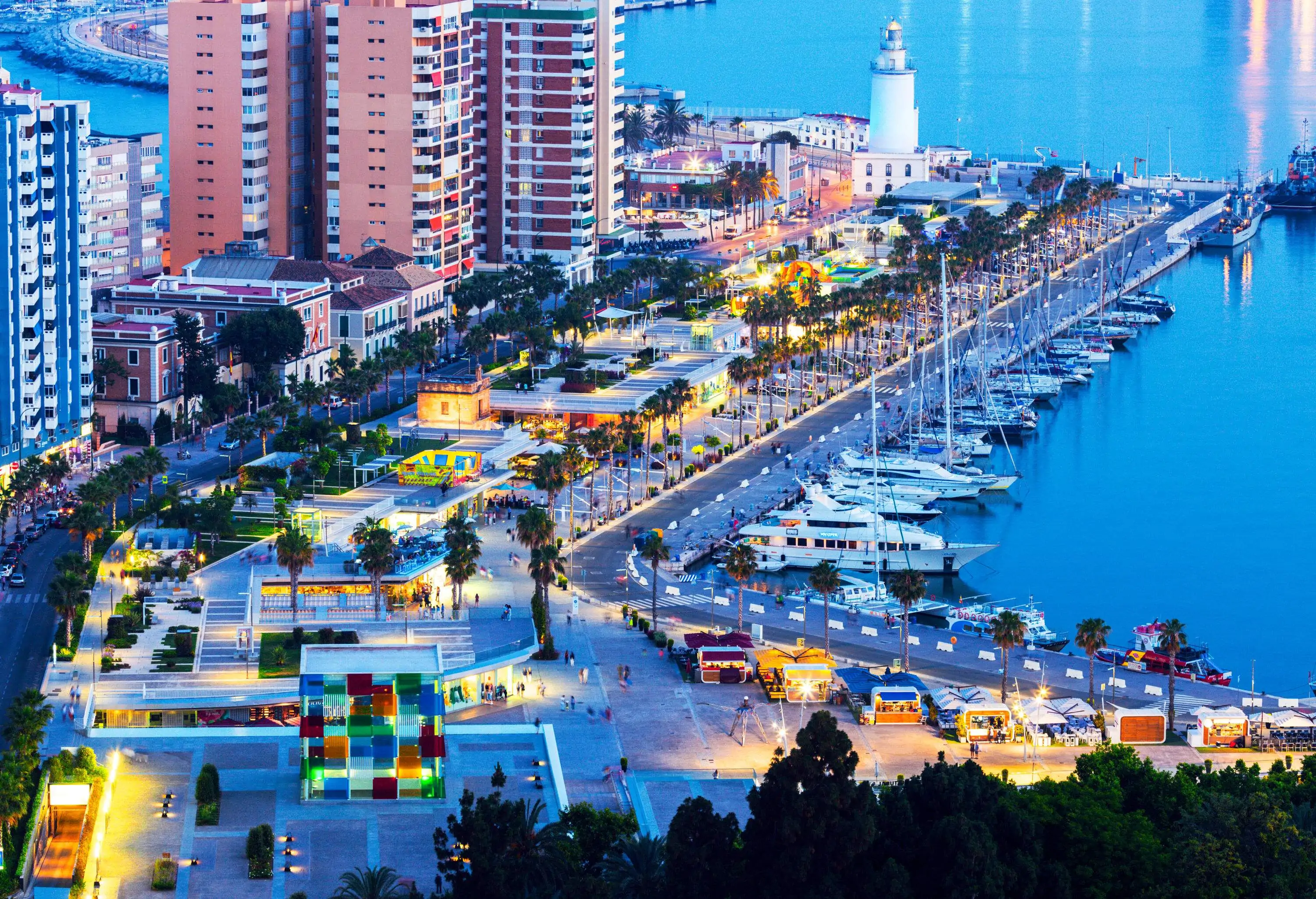 Aerial view of the illuminated road and tall buildings by the harbour with moored boats.