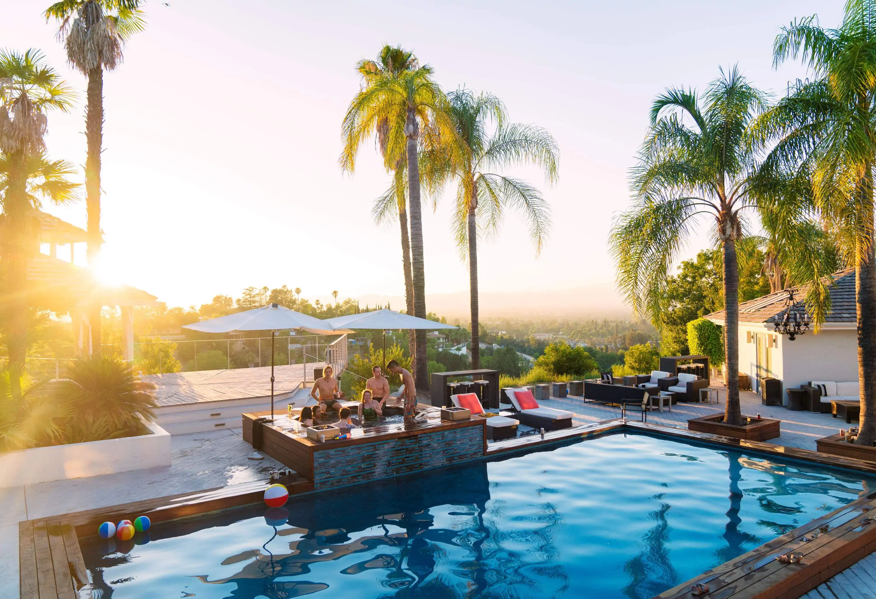 A group of friends enjoying a dip in a jacuzzi by the pool, with the blinding light of the sun streaming through the trees.