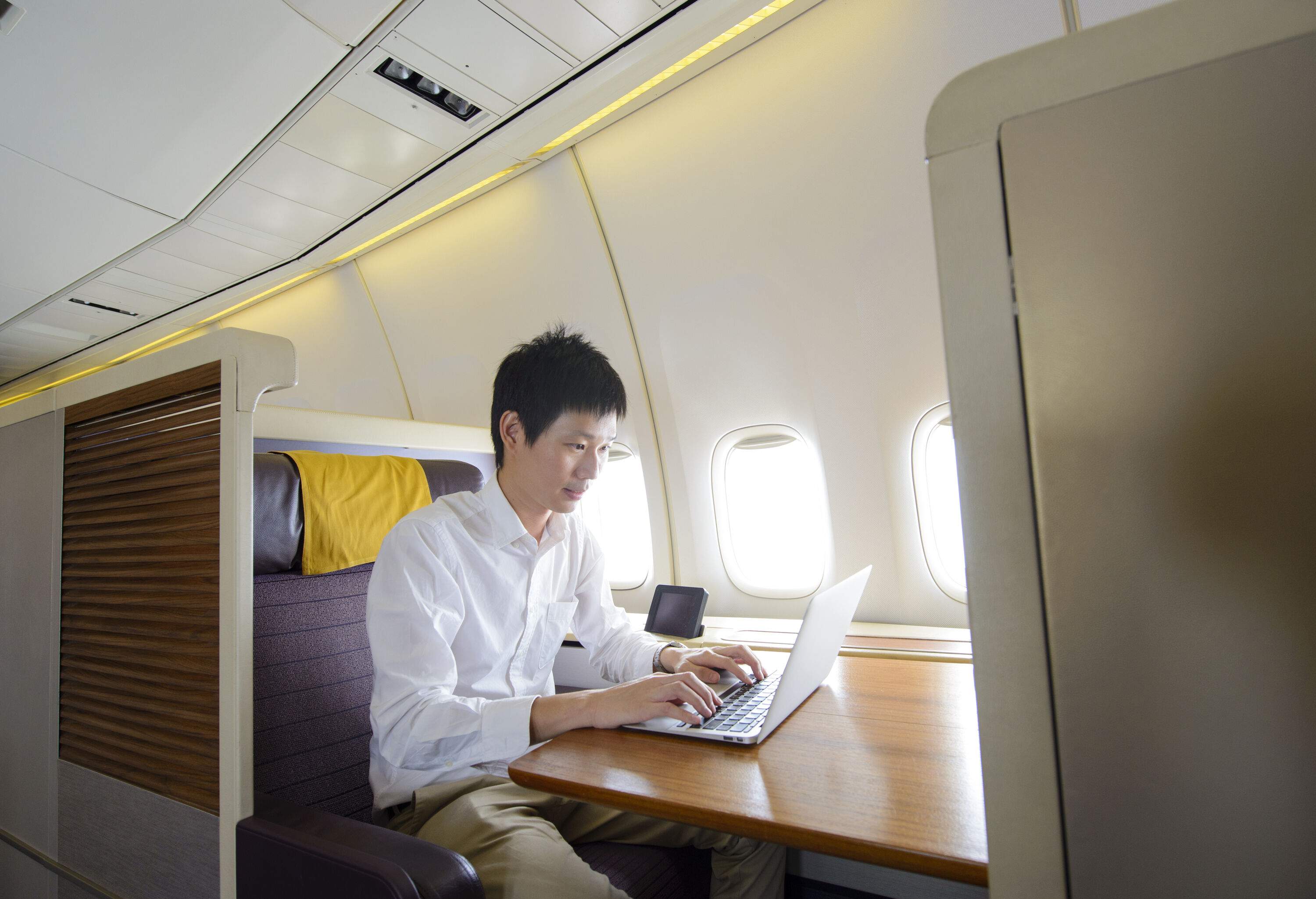 A businessman works on a laptop on a wooden table during a first-class flight.