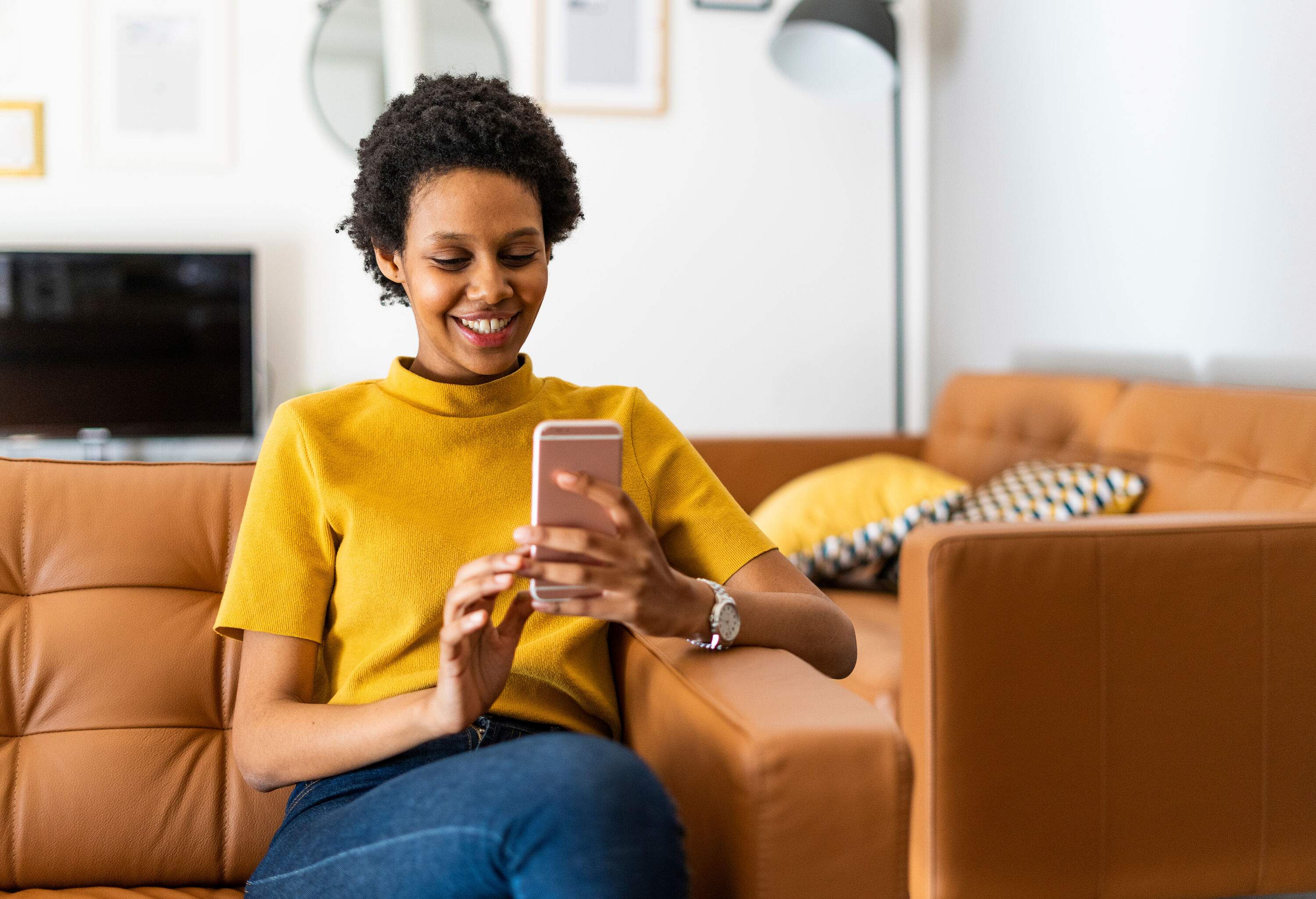 A short hair lady smiling while using her smartphone seated on the couch.