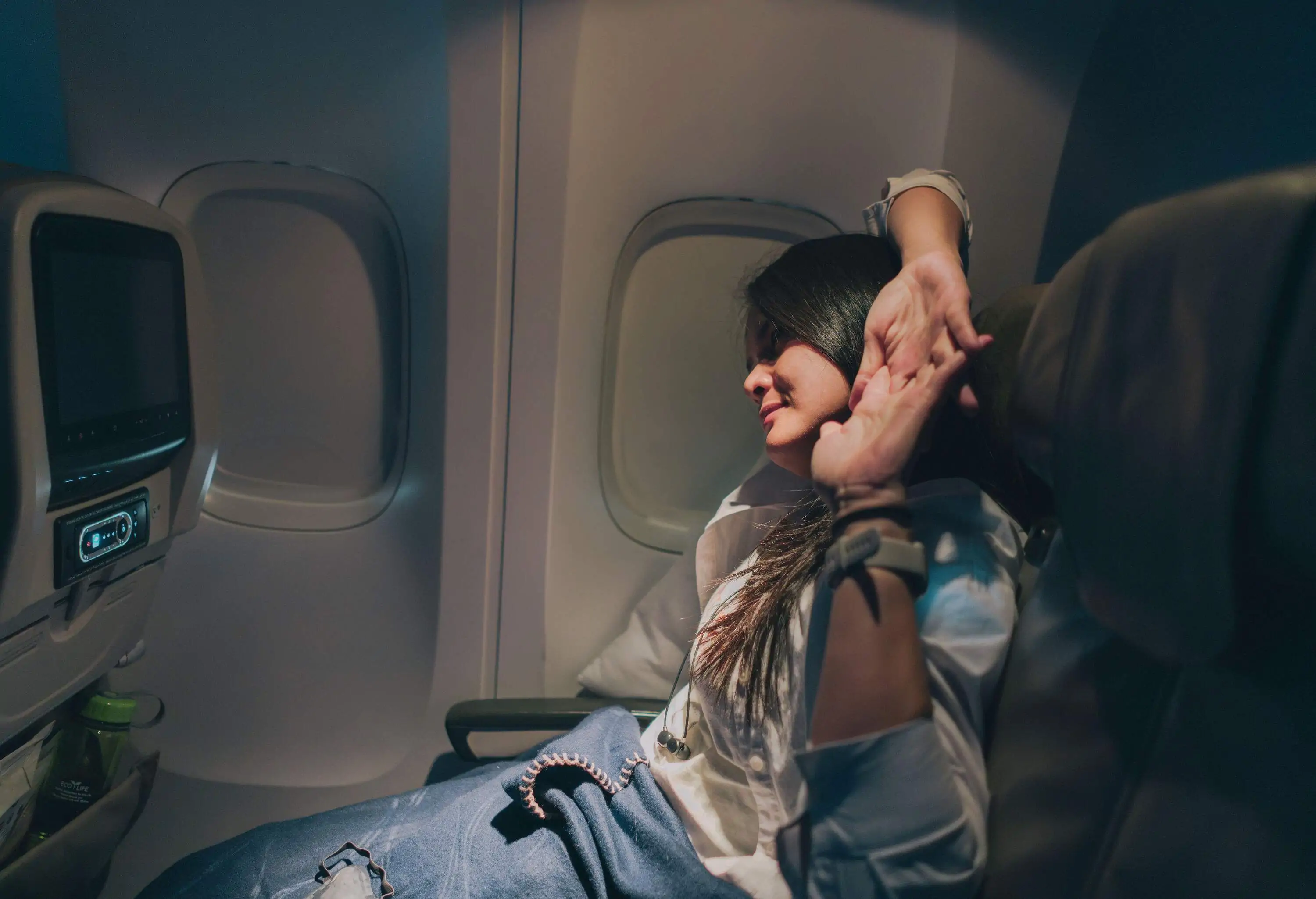 Young sleepy woman passenger stretching on the airplane